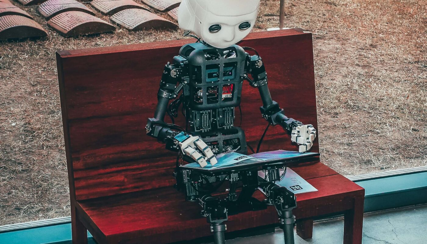 A humanoid robot sitting on a bench using a digital tablet, symbolizing the role of AI in design