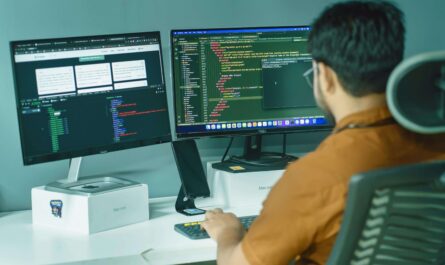 UI/UX designer working on mobile app layout using dual monitors and AI-assisted code editor interface